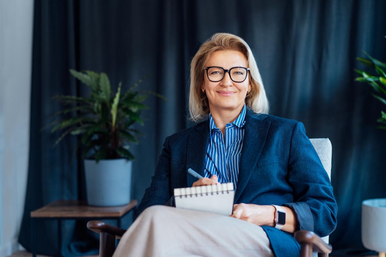 A behavioral healthcare professional sitting in an office smiling and holding a clipboard